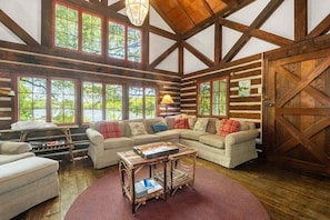 A log cabin interior with a large window, a sofa set, a coffee table, and a wooden door.