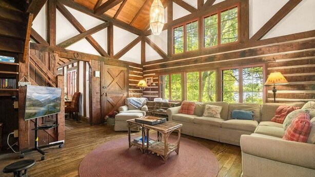 Ein Holzblockhaus-Interieur mit großem Fenster, einer Couch, einem Couchtisch und einem Fernseher.