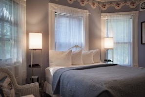 A bedroom with a bed, two bedside lamps, a chair, and a window with blinds. - Spacious Downtown Home • Pool • Walk to River & Attractions (Wisconsin Dells)