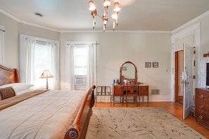A bedroom with a bed, a desk, a dresser, a mirror, and a chandelier.