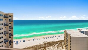 Un hôtel de grande hauteur surplombant une plage aux eaux turquoise et limpides, avec du sable fin et des parasols.