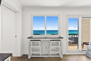 A room with a white desk, a view of the ocean through a window, and a sliding glass door leading to a balcony. - Perfect End of Summer Vacations at PP PH#31 (Panama City Beach)