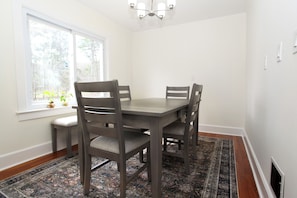 A dining room with a table and four chairs, a window with plants, and a patterned rug. - All Star Location with Views of Good Year Lake (Oneonta)
