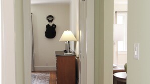 Een gang met houten vloeren, een deur naar een kamer met een lamp en een kapstok.