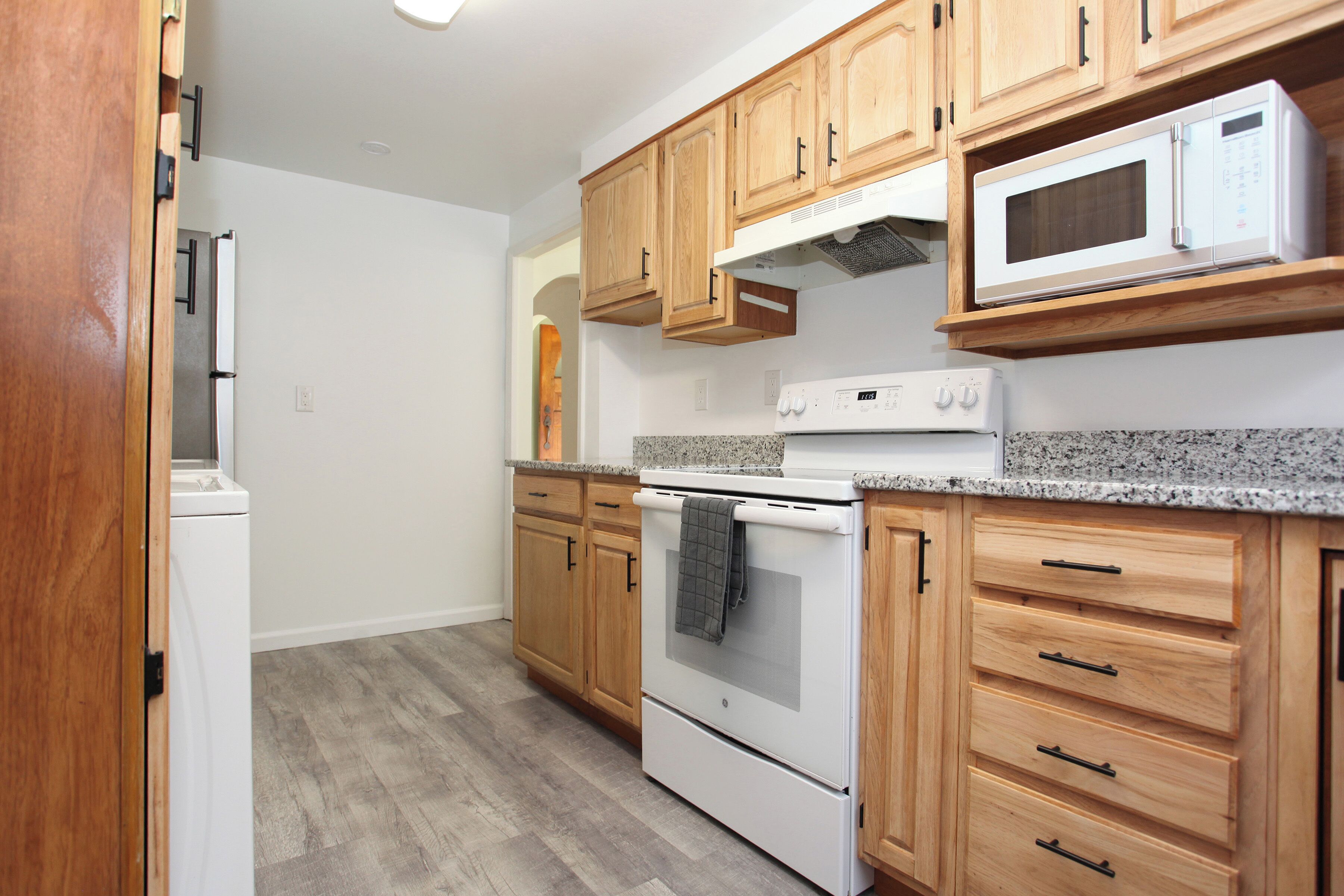 Una cocina con armarios de madera, estufa blanca, microondas y refrigerador.