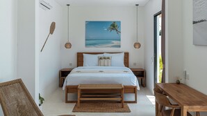 A bedroom with a bed, bedside tables, a wooden bench, a dining table, and a view of the beach. - Villa Irena (Canggu)