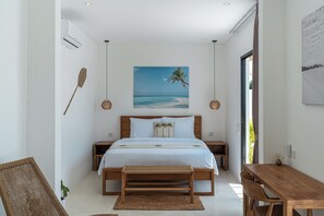 A bedroom with a bed, bedside tables, a wooden bench, a dining table, and a view of the beach. - Villa Irena (Canggu)