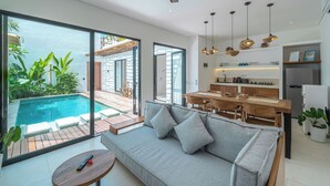 A modern living space with a pool, a sofa, a dining area, and a kitchen. - Villa Irena (Canggu)