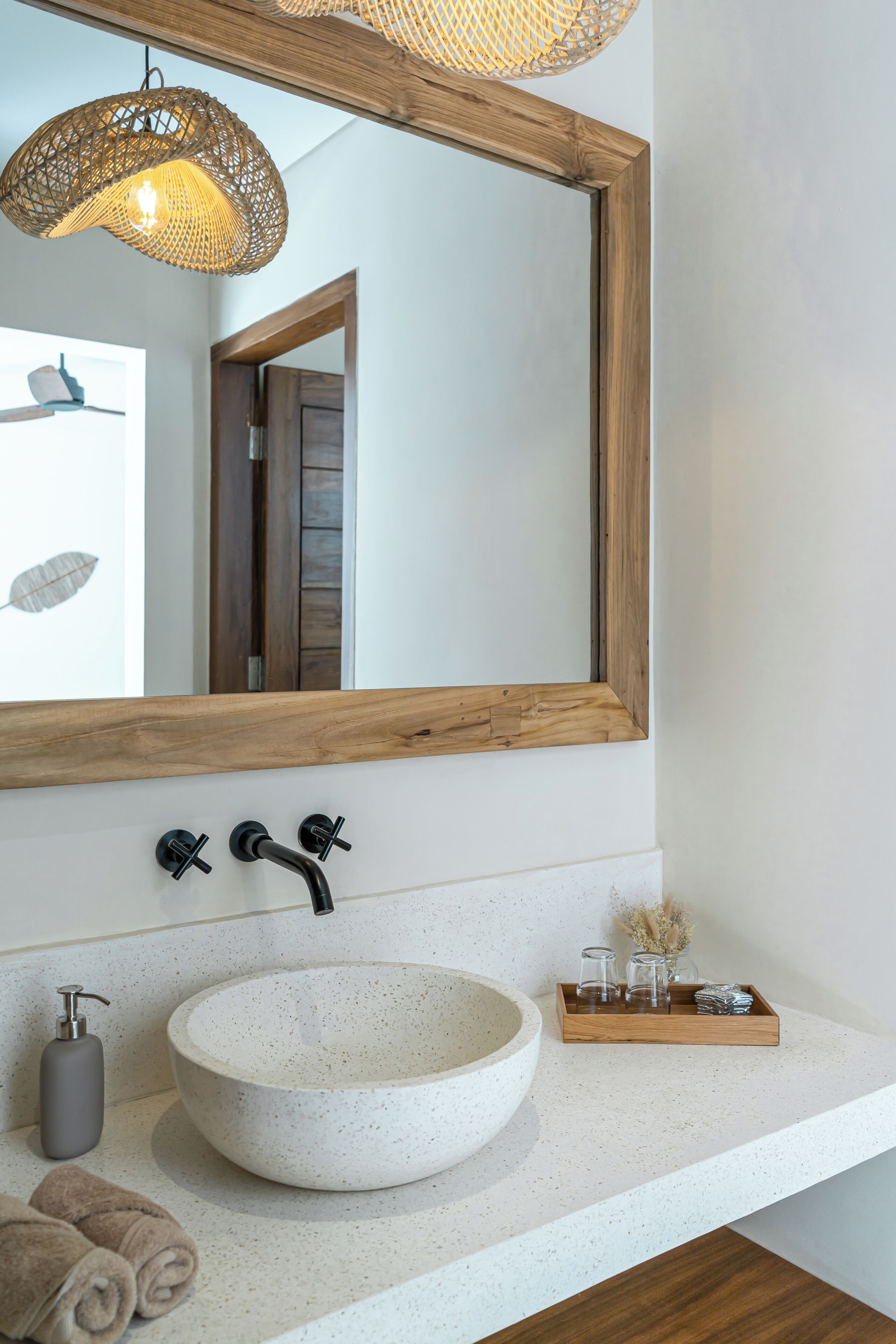 Un baño con lavamanos de piedra redonda, espejo con marco de madera y lámpara colgante.