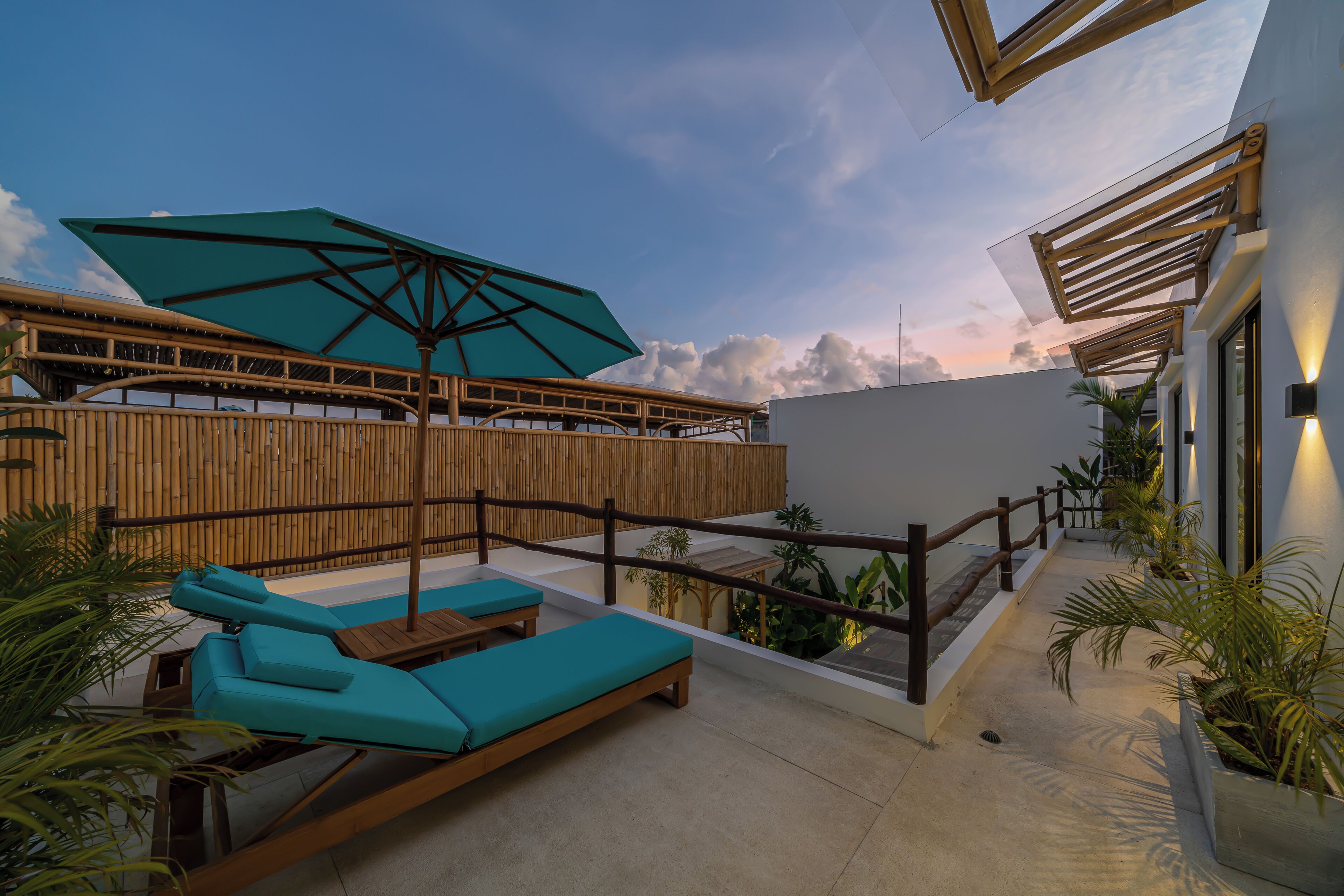 A rooftop terrace with wooden loungers, a large umbrella, and potted plants.