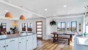 Une cuisine moderne avec des meubles blancs, un plan de travail en bois, des luminaires suspendus et une grande fenêtre offrant une vue dégagée.