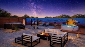 Une terrasse extérieure avec une vue sur un ciel étoilé, une fresque murale, un jacuzzi et des sièges d’extérieur.