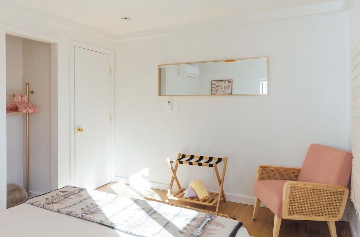Een kamer met een bed, een stoel, een klein tafeltje, een spiegel en een deur.