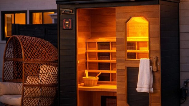 Un sauna avec une façade en bois, une grande fenêtre et une serviette accrochée à la porte.