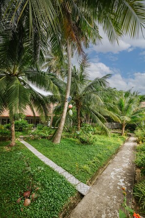A pathway flanked by lush greenery and palm trees, leading to a building with a tiled roof. - Terrace Resort (Phu Quoc)
