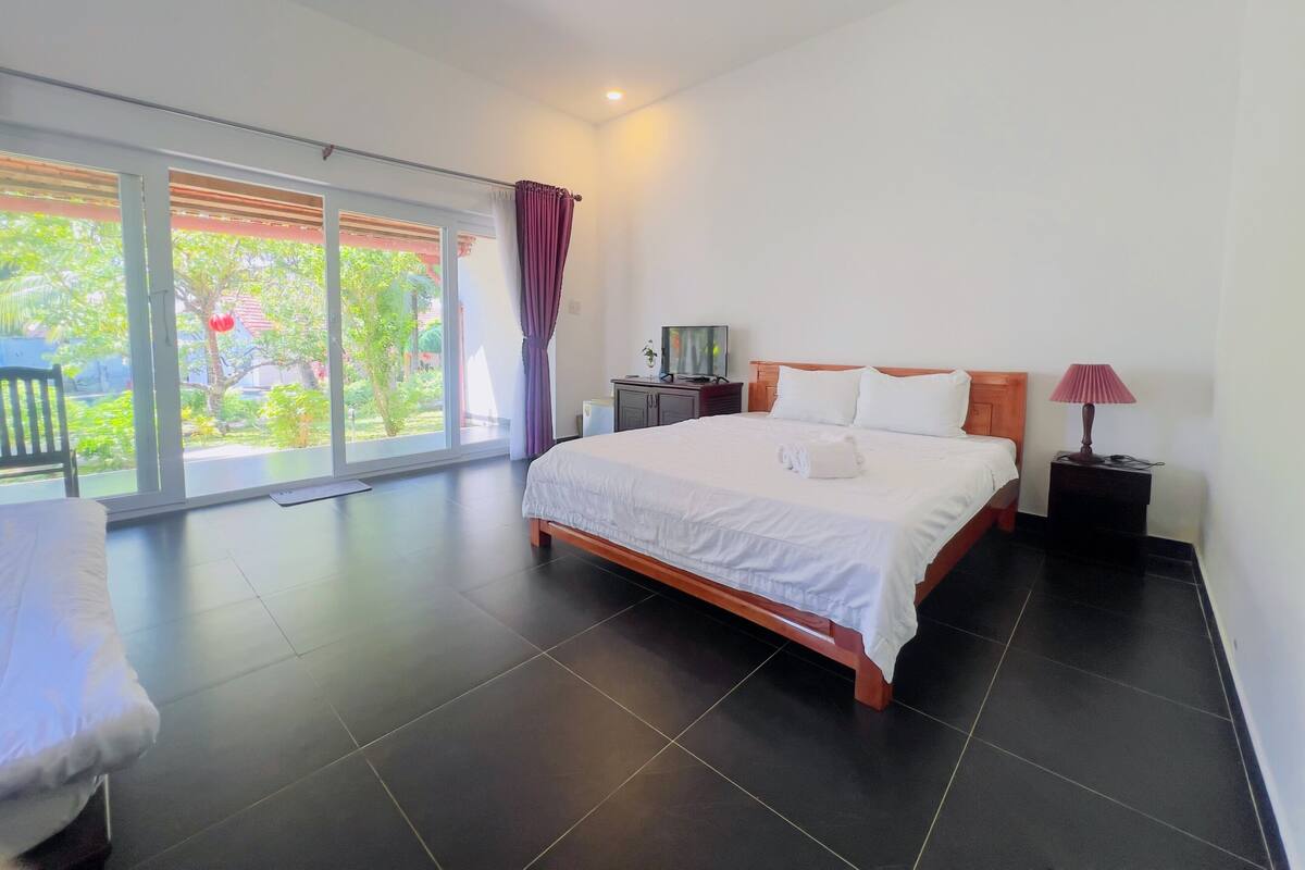 A bedroom with a bed, a nightstand, a lamp, a chair, and a sliding glass door leading to a balcony.