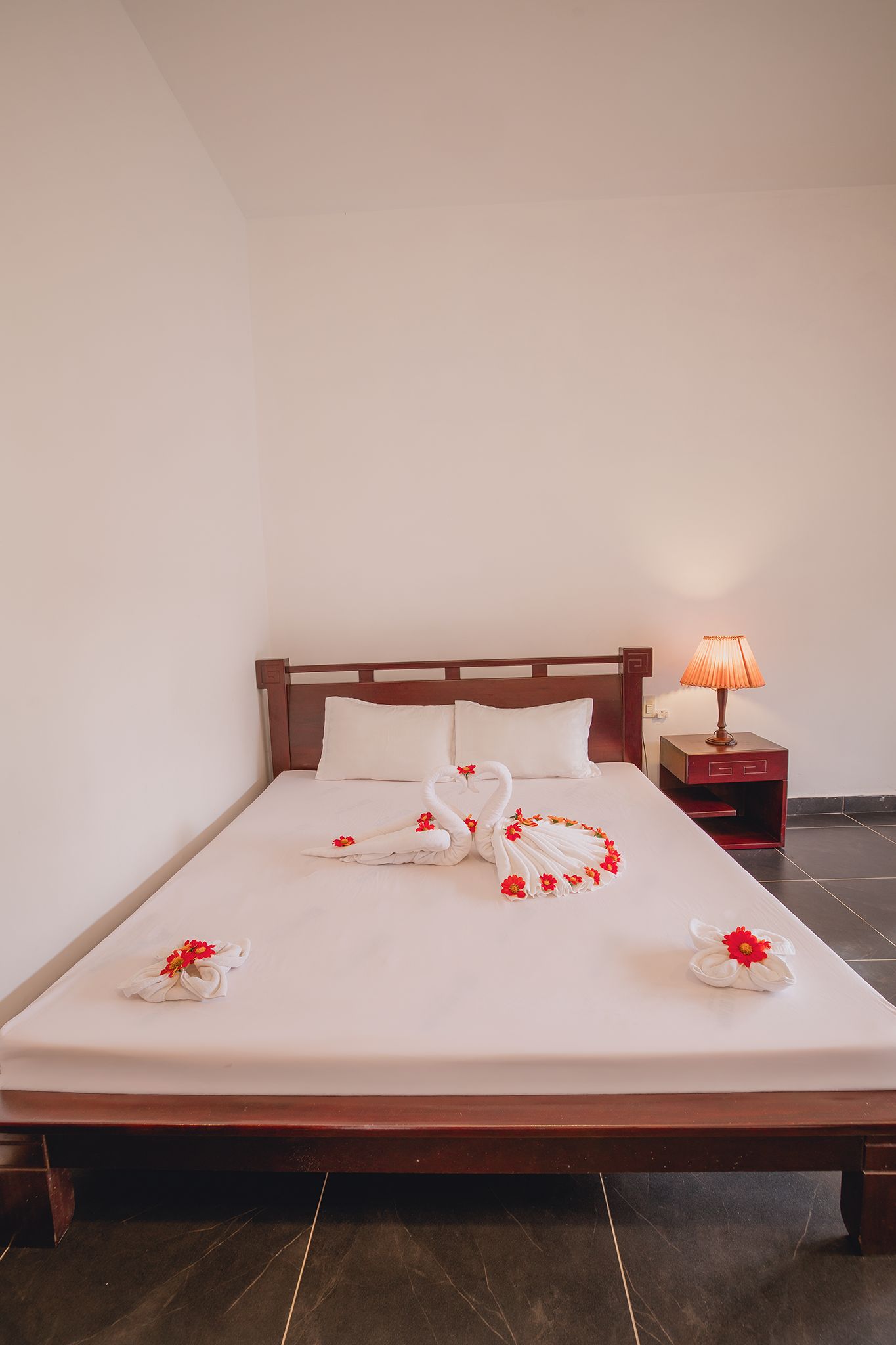 Una cama bien tendida con cabecera de madera, una lámpara de noche y toallas decorativas dispuestas en forma de cisne.