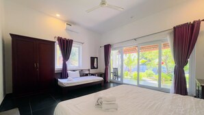 Ein Hotelzimmer mit einem großen Bett, einem Schreibtisch, einem Kleiderschrank, einem Deckenventilator und Blick ins Freie.