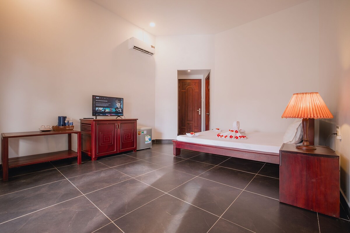 A hotel room with a bed, a television, a wooden cabinet, a small table, and a lamp.