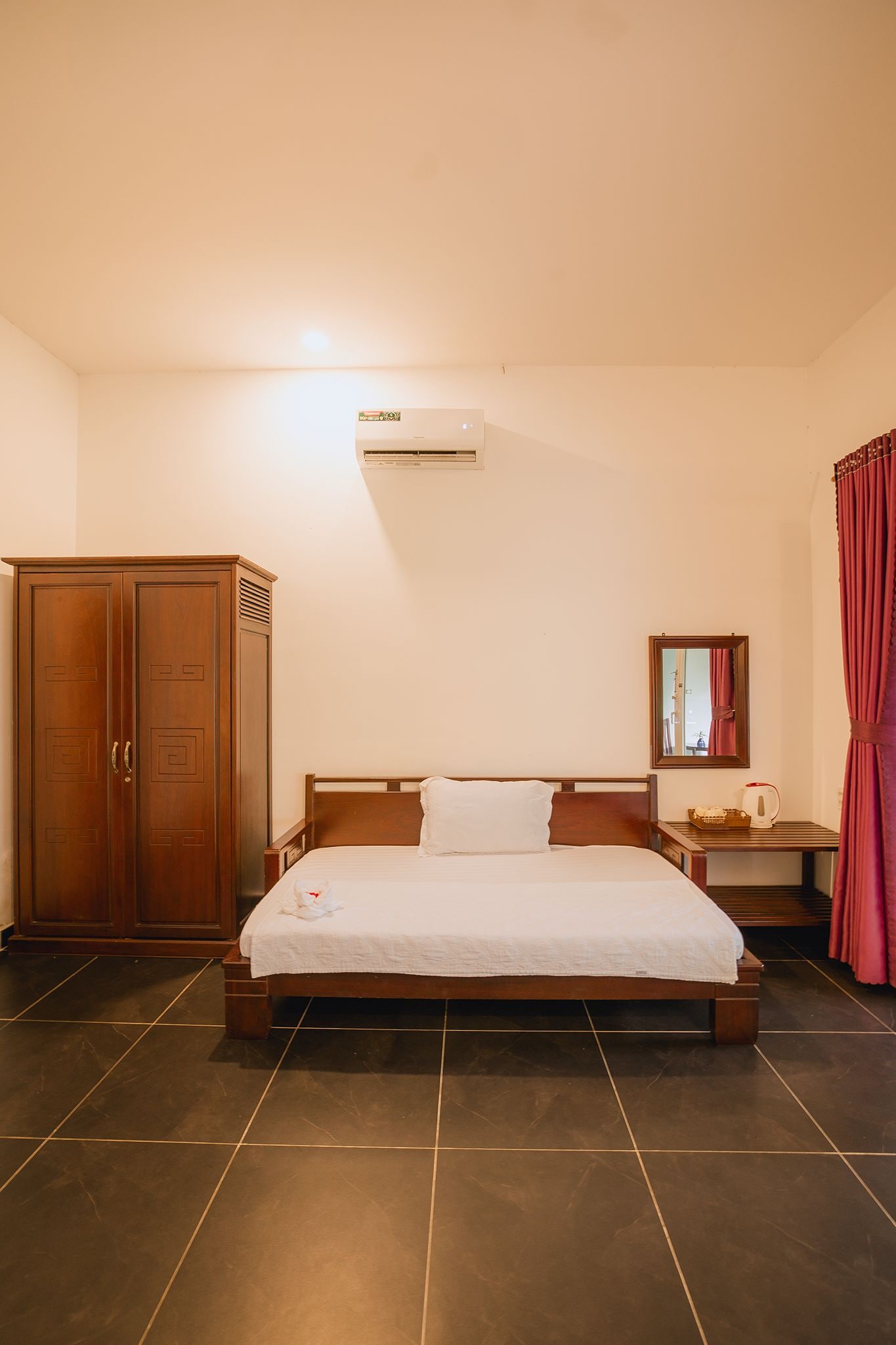 Una camera d'albergo con un letto, un armadio, un comodino, uno specchio e un condizionatore d'aria.