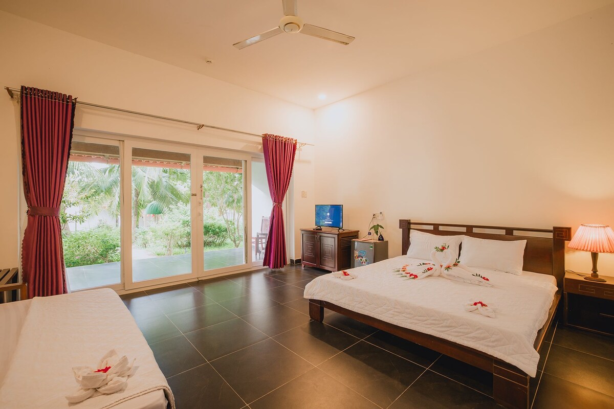 A hotel room with a bed, a desk, a television, and a view of greenery through the windows.