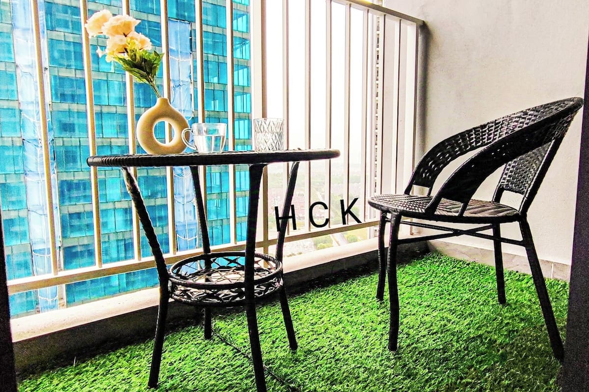 Un balcon avec une table et une chaise, un vase rempli de fleurs et une vue sur un immeuble aux fenêtres bleues.