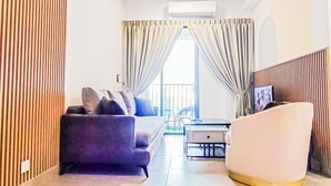 A modern living room with a sofa, a white chair, a small table, and a view through a glass door. - Mall Suite at Sunsuria Forum by HCK (Shah Alam)