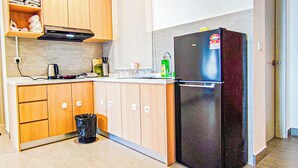 A compact kitchen with wooden cabinets, a black refrigerator, a kettle, and a trash bin. - Mall Suite at Sunsuria Forum by HCK (Shah Alam)