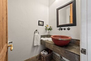 Ein Badezimmer mit Holztür, einem roten Waschbecken, einem Spiegel, einem Handtuchhalter und einem kleinen Bilderrahmen an der Wand.
