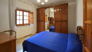 Une chambre à coucher avec un lit, une armoire en bois, un bureau et une fenêtre avec des rideaux.