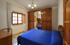Ein Schlafzimmer mit einem Bett, einem Holzschrank, einem Schreibtisch und einem Fenster mit Vorhängen.