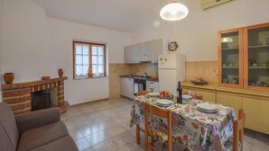 Une cuisine avec une table à manger pour deux personnes, une cheminée et une fenêtre ornée de rideaux en dentelle.