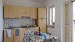 Una cocina con armarios de madera, salpicadero de azulejos, estufa a gas y una mesa de comedor preparada con platos, vasos y una botella.