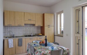 A kitchen with wooden cabinets, a tiled backsplash, a gas stove, and a dining table set with plates, glasses, and a bottle. - Lovely apartment in Ricadi with swimming pool (Ricadi)