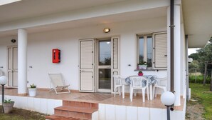 Un espacio al aire libre cubierto con una mesa y sillas, un extintor rojo y una ventana con contraventanas.