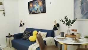 A modern living room with a blue sofa, a yellow duck plush toy, a dining table with a white tablecloth, and a painting on the wall. - Makati City Central Stay Apartments (Makati)