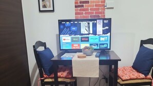 A room with a desk, two chairs, a computer monitor displaying streaming services, and a small plant on the desk. - Makati City Central Stay Apartments (Makati)