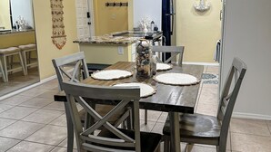Zona pranzo con tavolo e sedie in legno, una lampada a sospensione e una cucina sullo sfondo.