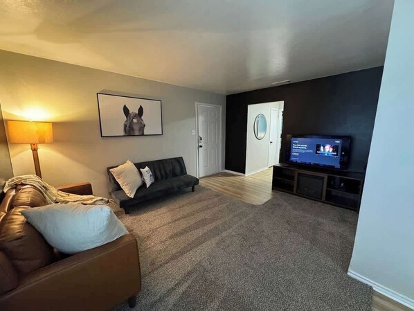 Ein Wohnzimmer mit einer Couch, einem Fernseher, einem gerahmten Bild an der Wand und einer Tür.