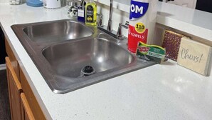 Una cocina con un lavamanos doble, una cafetera, una botella de jabón para manos y una caja de toallas de papel.