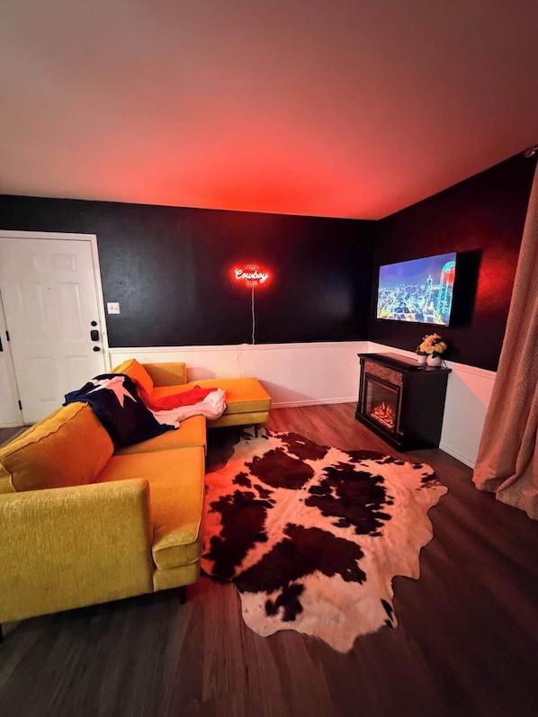 Olohuone, jossa on sohva, televisio, takka ja neonvalomainos.