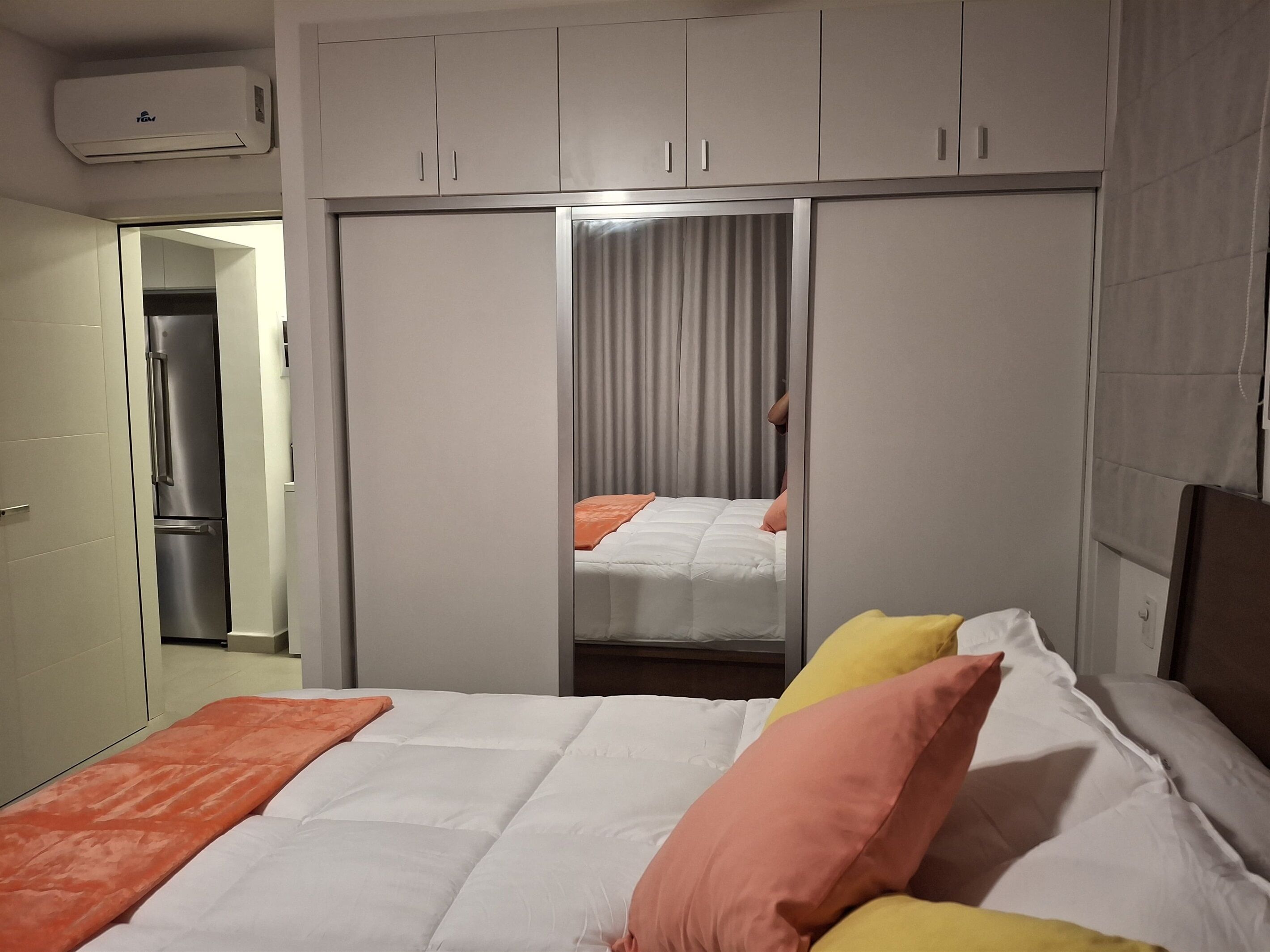 A bedroom with a bed, a wardrobe, and an air conditioning unit.