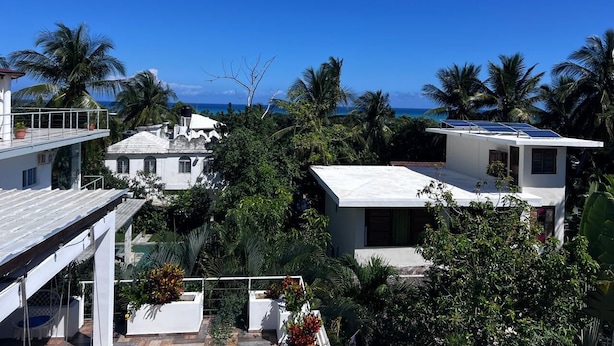 A coastal residential area with white buildings, a view of the ocean, and palm trees. - Surf View Penthouse @ Encuentro (Cabarete)