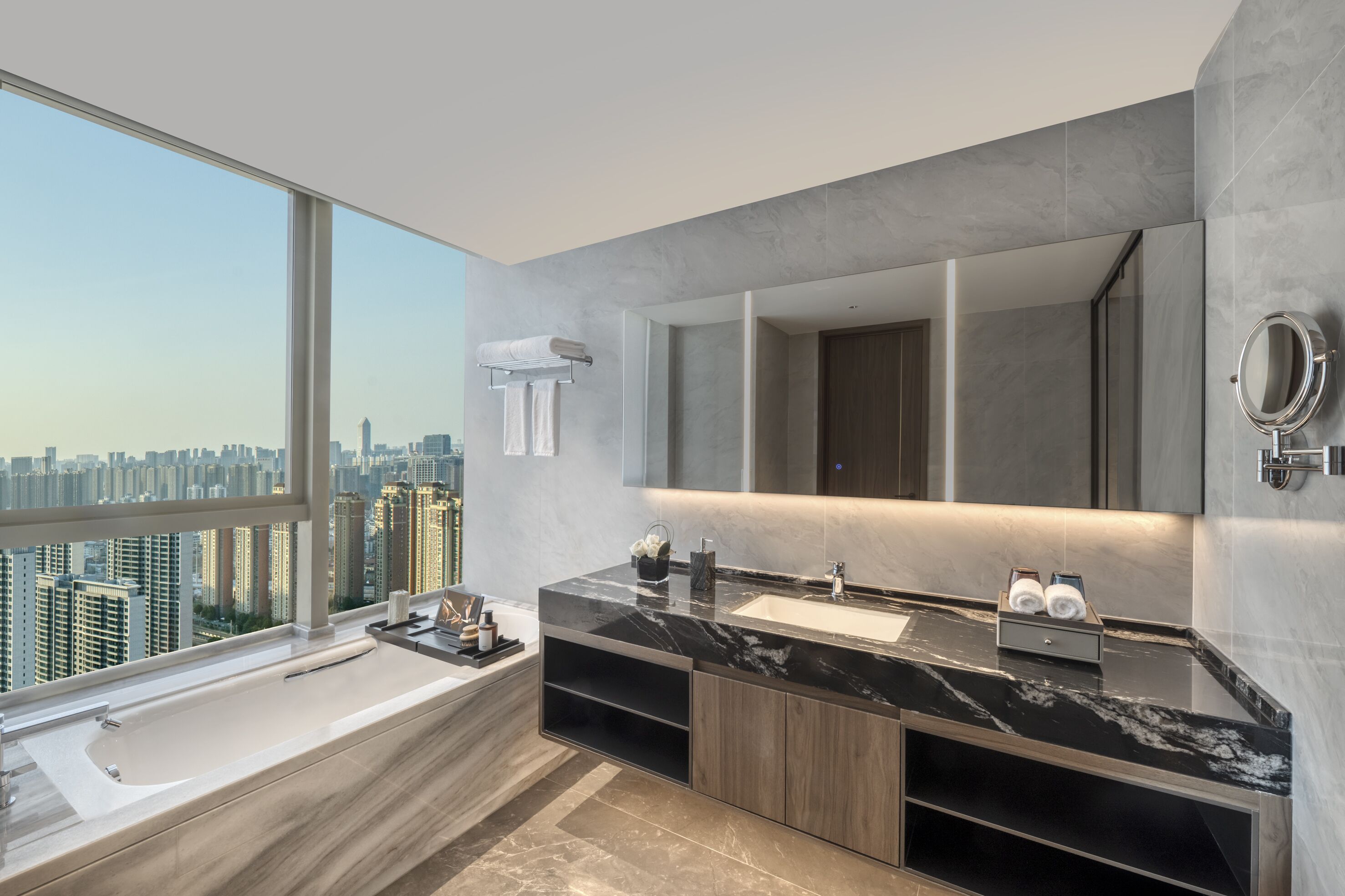 Ein modernes Badezimmer mit großem Fenster, einer Badewanne, einem Waschtisch mit Spiegel und Blick auf die Stadt.
