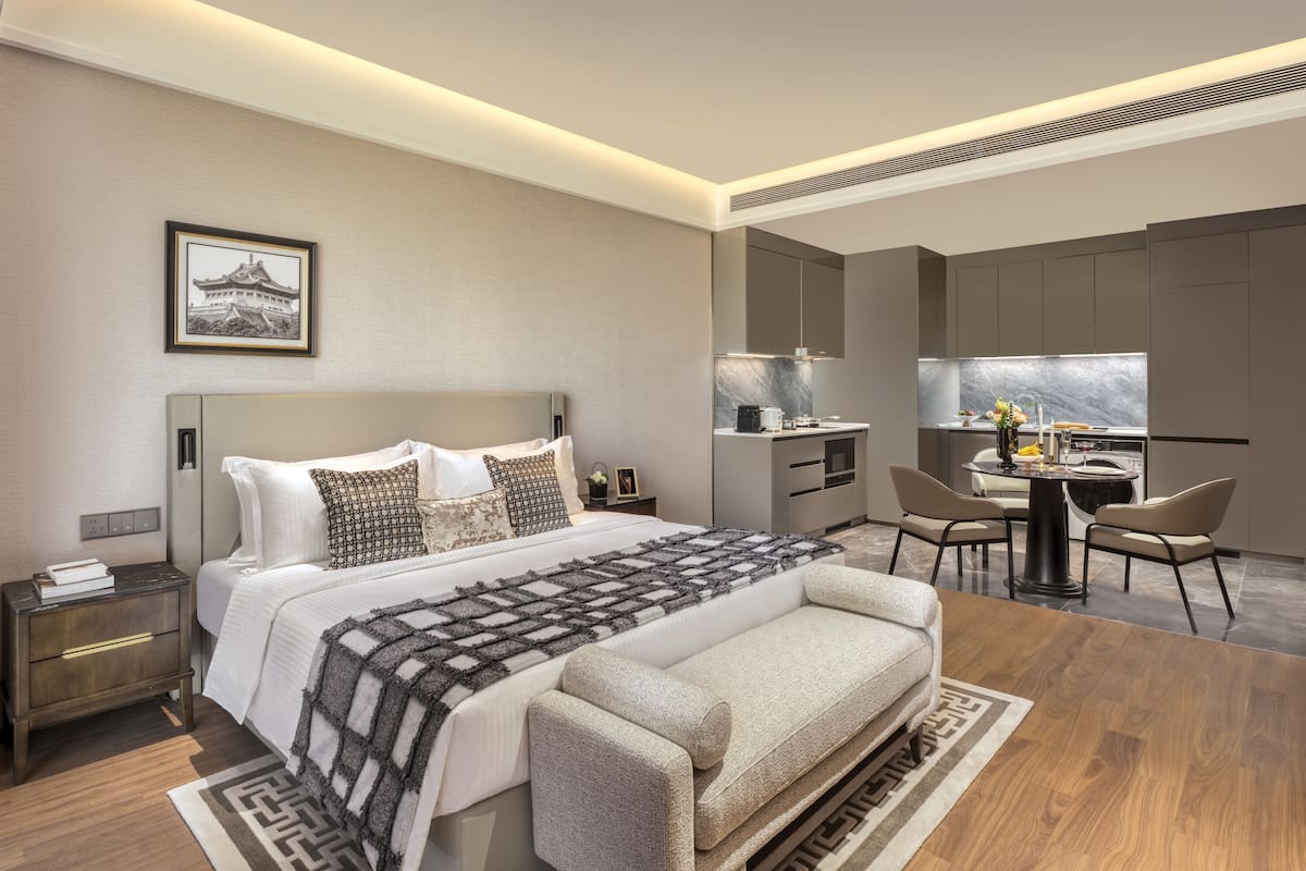 A modern bedroom with a large bed, bedside tables, a desk, and a view of the city.