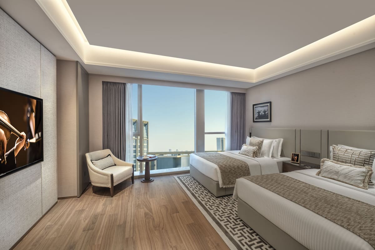 A modern hotel room with a large bed, a smaller bed, a sofa, a TV, and a balcony with a city view.