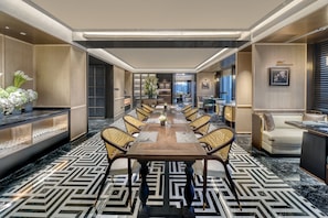 Una larga mesa de comedor con sillas, un sofá y un televisor en una habitación de hotel moderna.