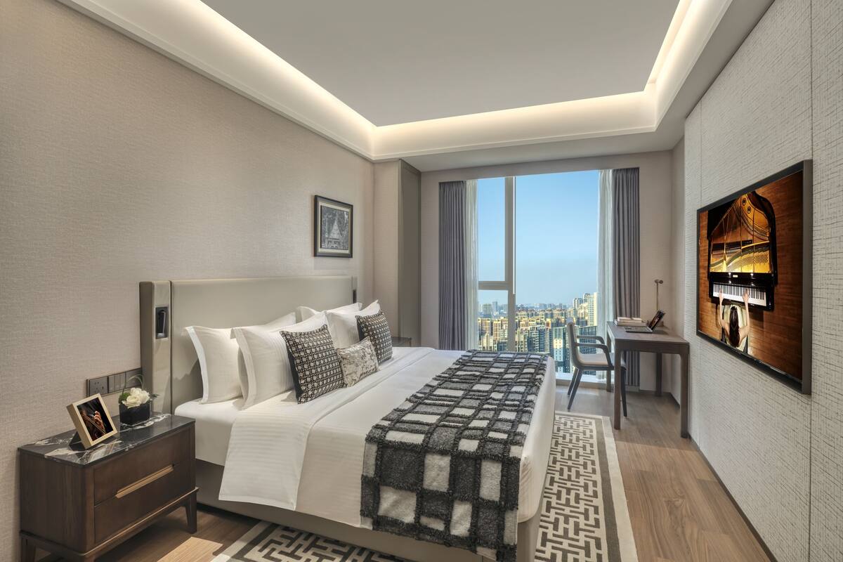 A modern hotel room with a large bed, a desk, a TV, and a city view.