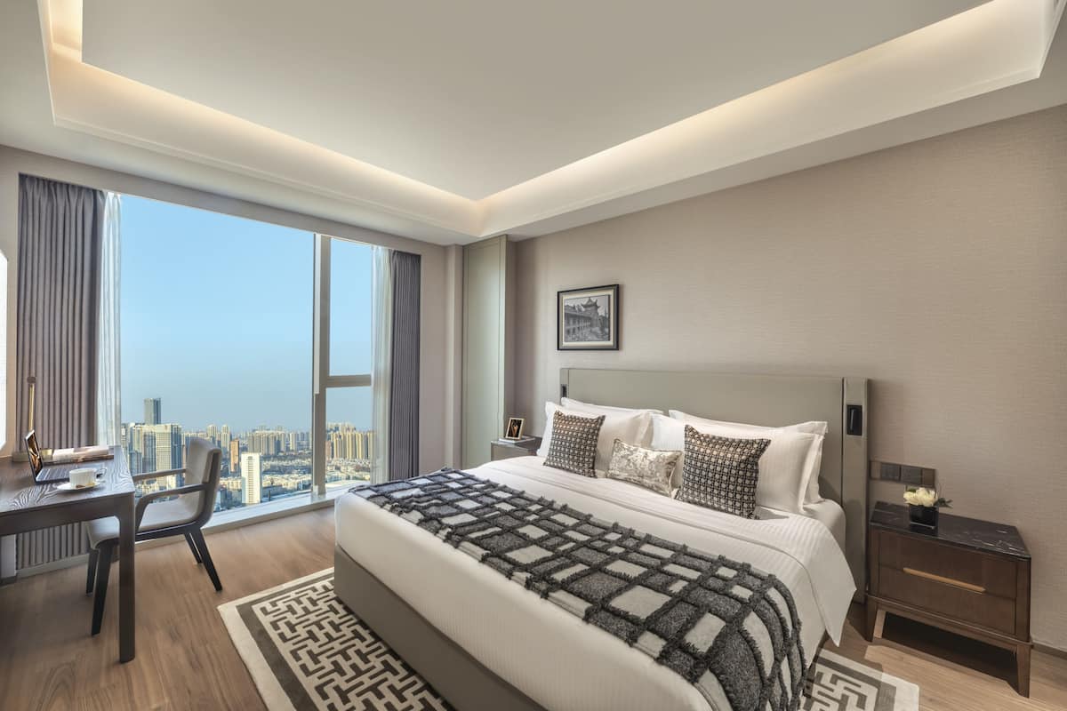 A modern hotel room with a large bed, a desk, and a view of the city.