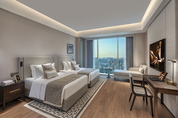 A modern hotel room with two beds, a desk, a chair, a TV, and a city view.